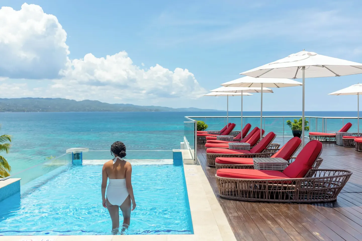 Guest entering the infinity pool beside red loungers at S Hotel Montego Bay.