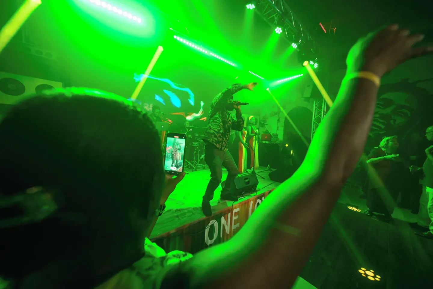 Live performer on a green-lit stage with guests dancing at S Hotel Montego Bay.