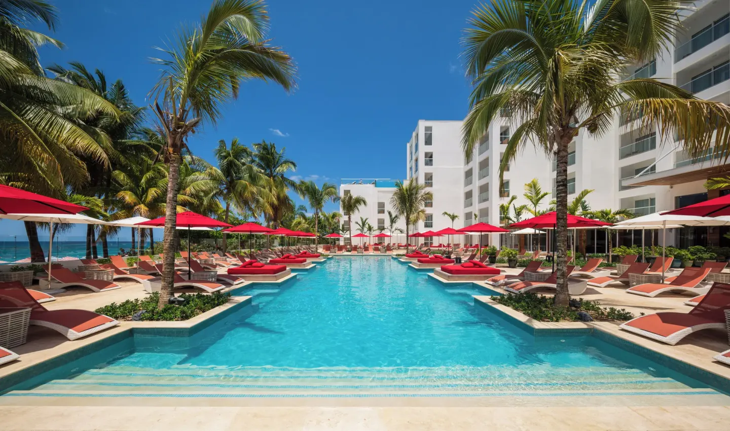 Long pool with red loungers and umbrellas between palms at S Hotel Montego Bay.