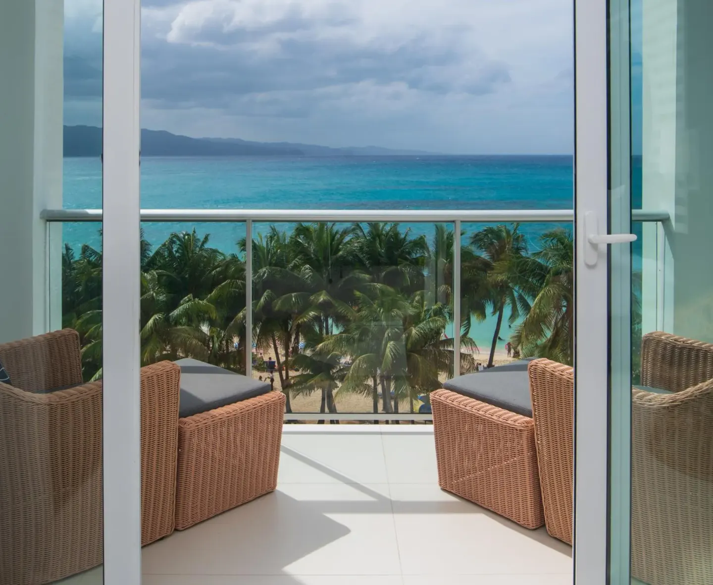 Balcony with wicker chairs overlooking palms and the sea at S Hotel Montego Bay.
