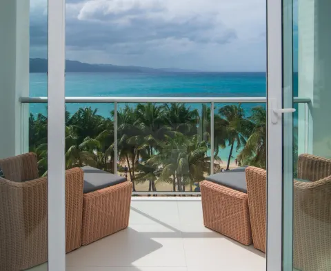 Balcony with wicker chairs overlooking palms and the sea at S Hotel Montego Bay.