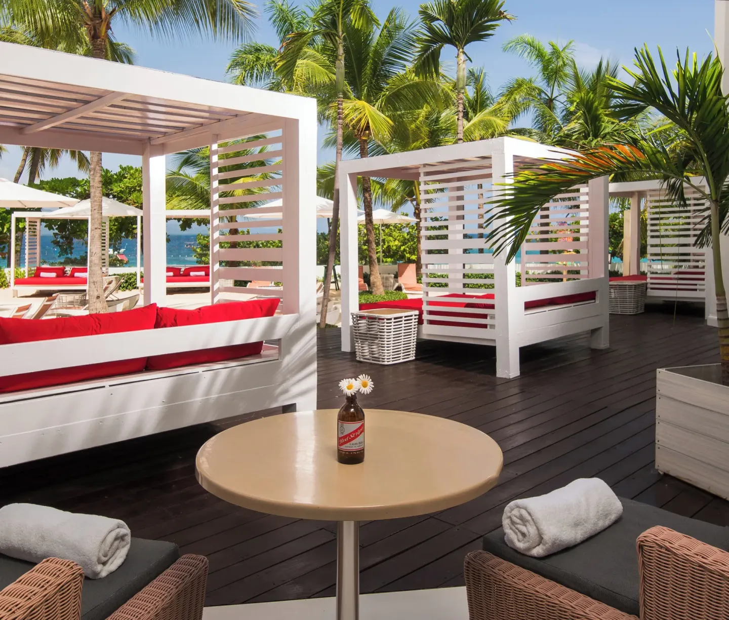 Poolside cabanas with red cushions and palms near the beach at S Hotel Montego Bay.