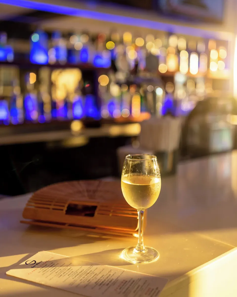 Wine glass on a bar counter with softly lit bottles behind it at S Hotel Montego Bay.