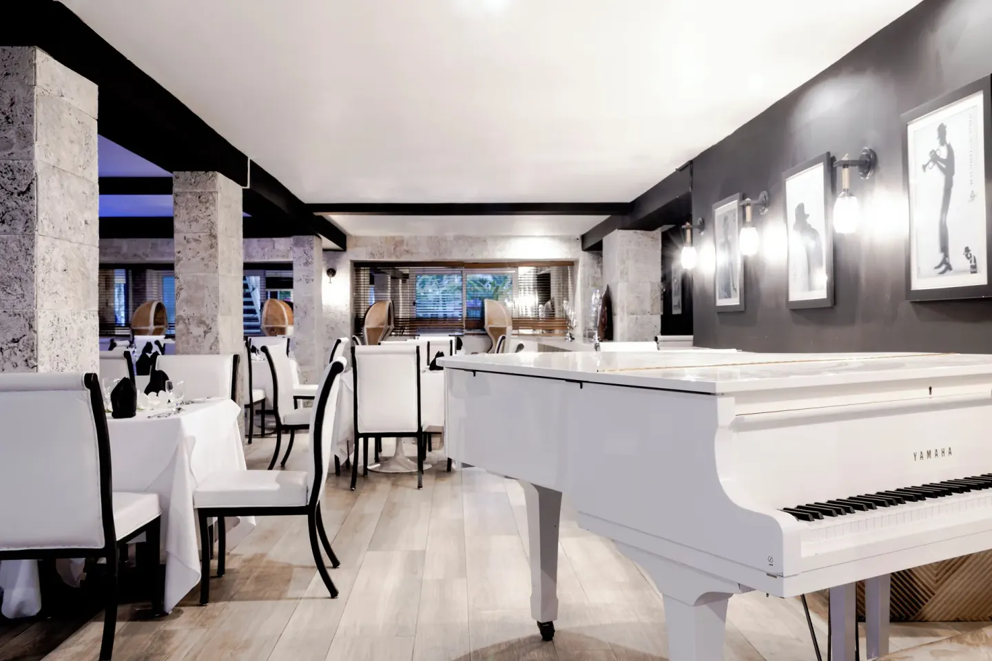 Dining room with a white grand piano and framed art at S Hotel Montego Bay.