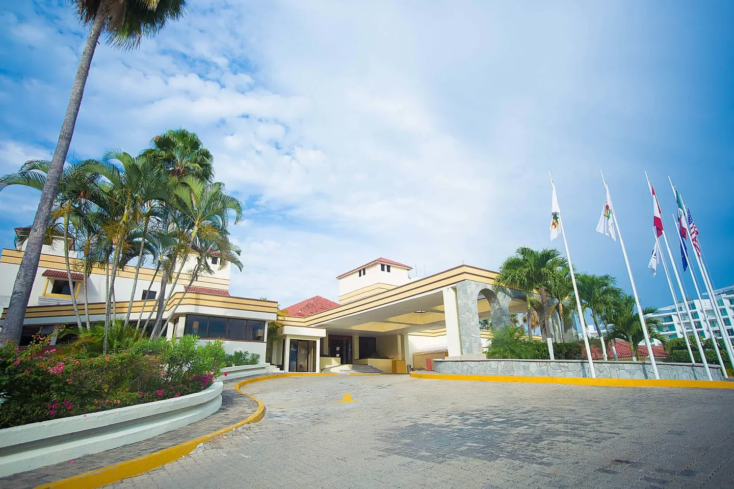 Covered entrance drive with palms, flags, and landscaped beds at Samba Vallarta.