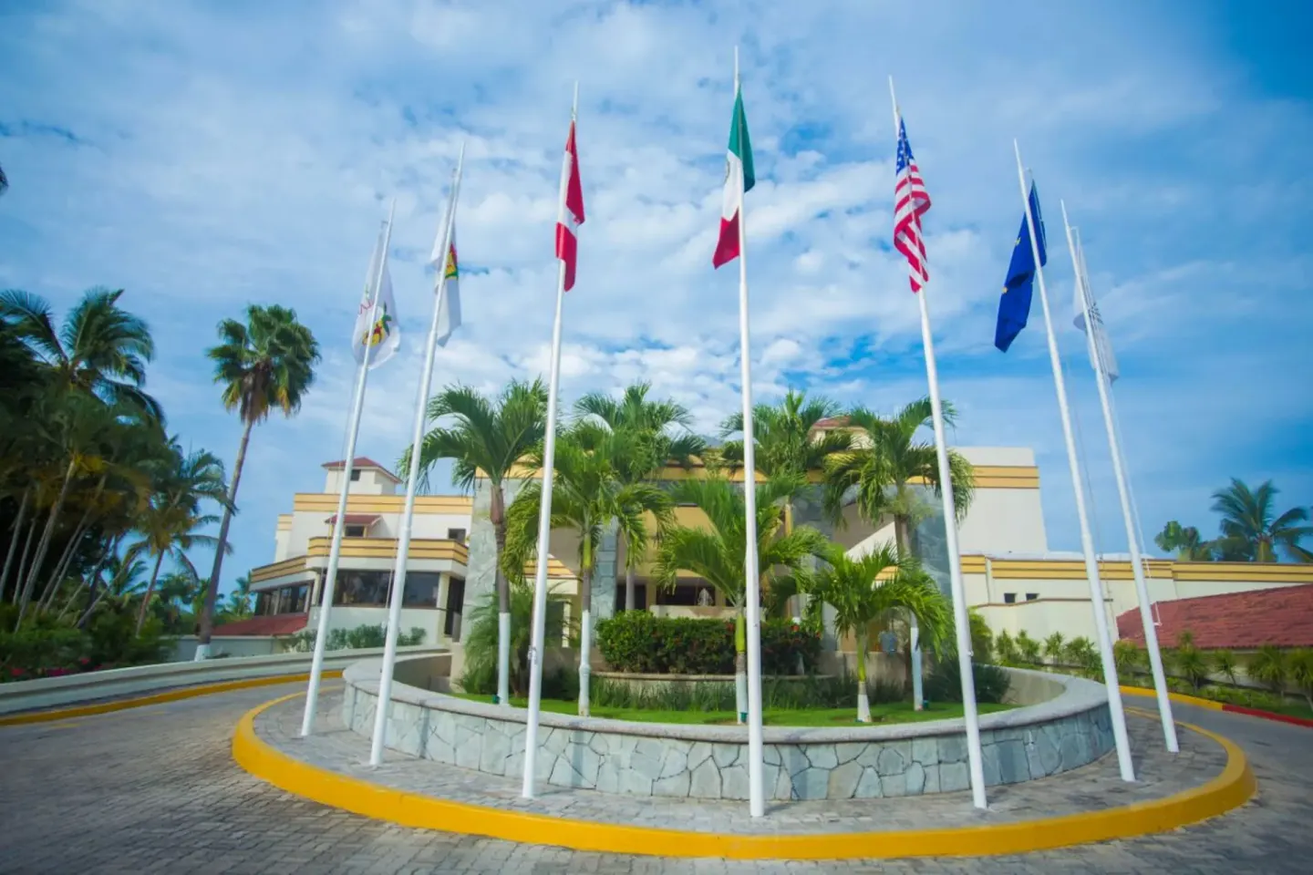 Flagpoles in a circular driveway with palms and resort buildings at Samba Vallarta.