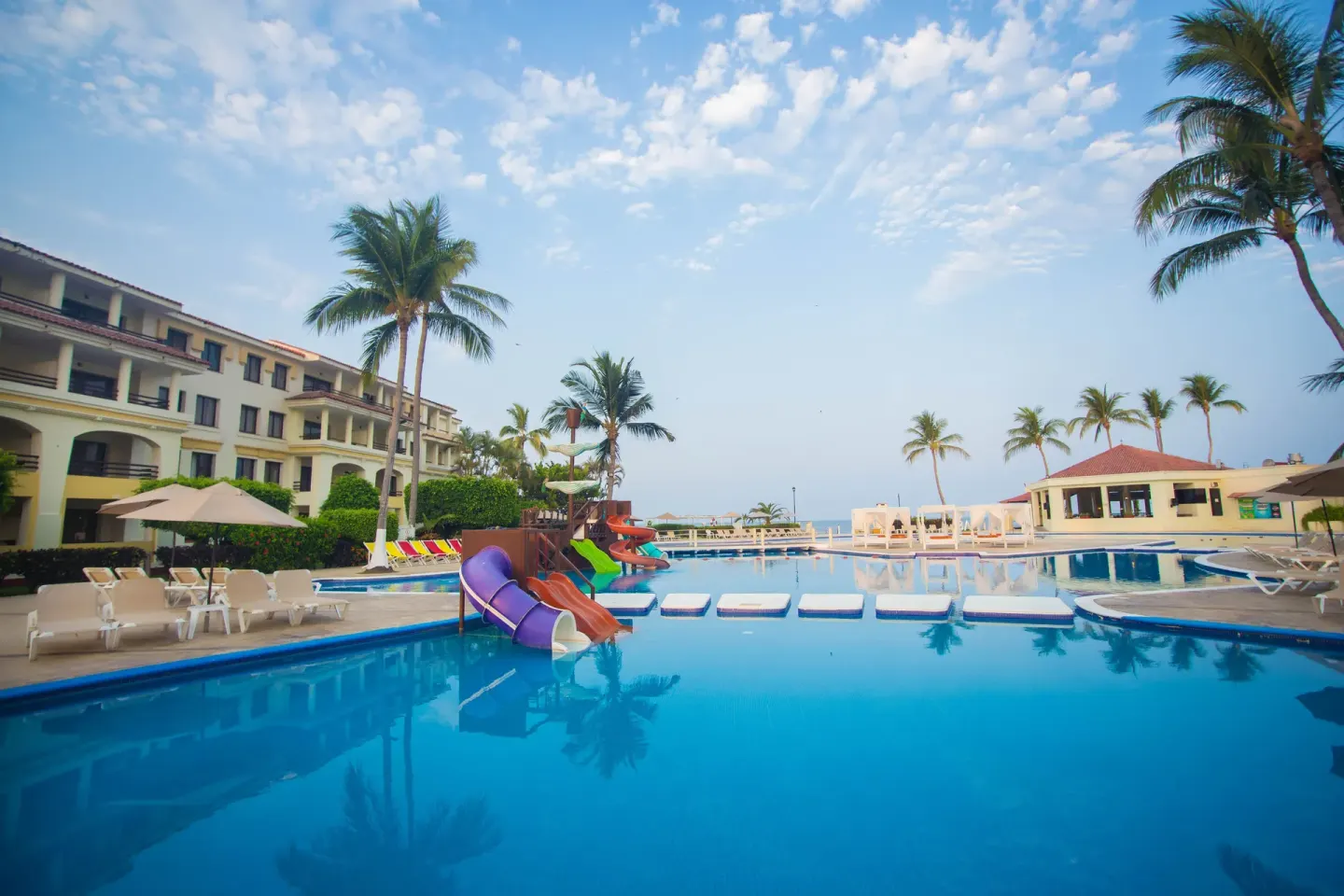 Main pool with slides, loungers, and palm trees at Samba Vallarta.