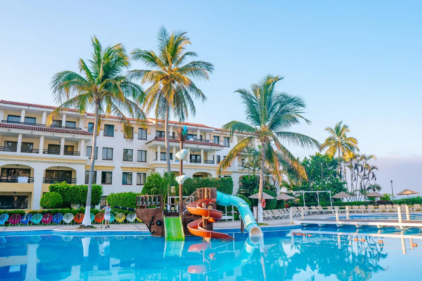 Pool with colorful slides, palms, loungers, and guest buildings at Samba Vallarta.