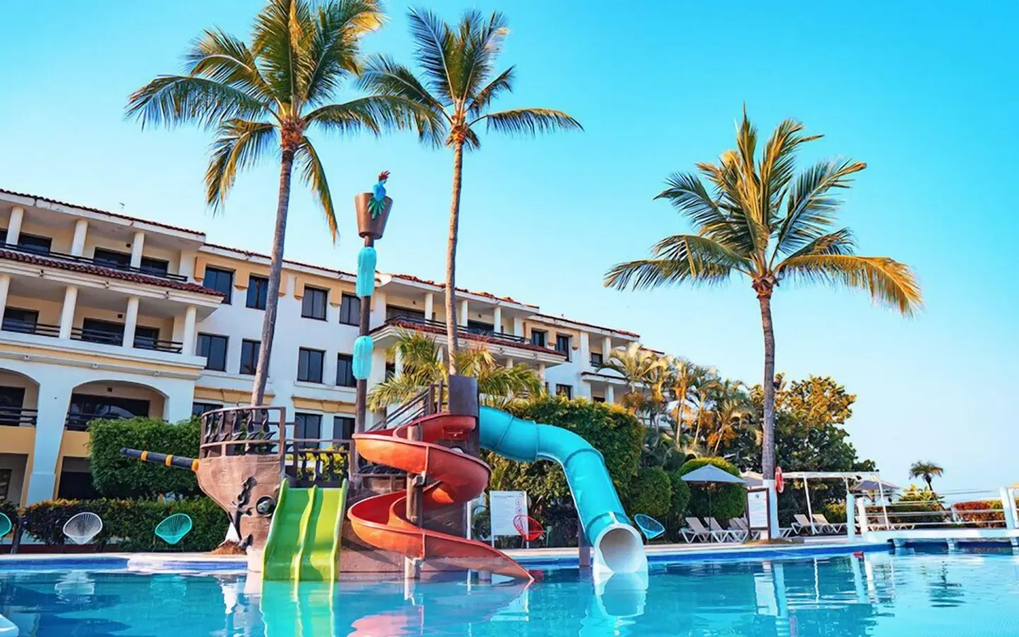 Pool with colorful waterslides, palm trees, and resort building at Samba Vallarta.