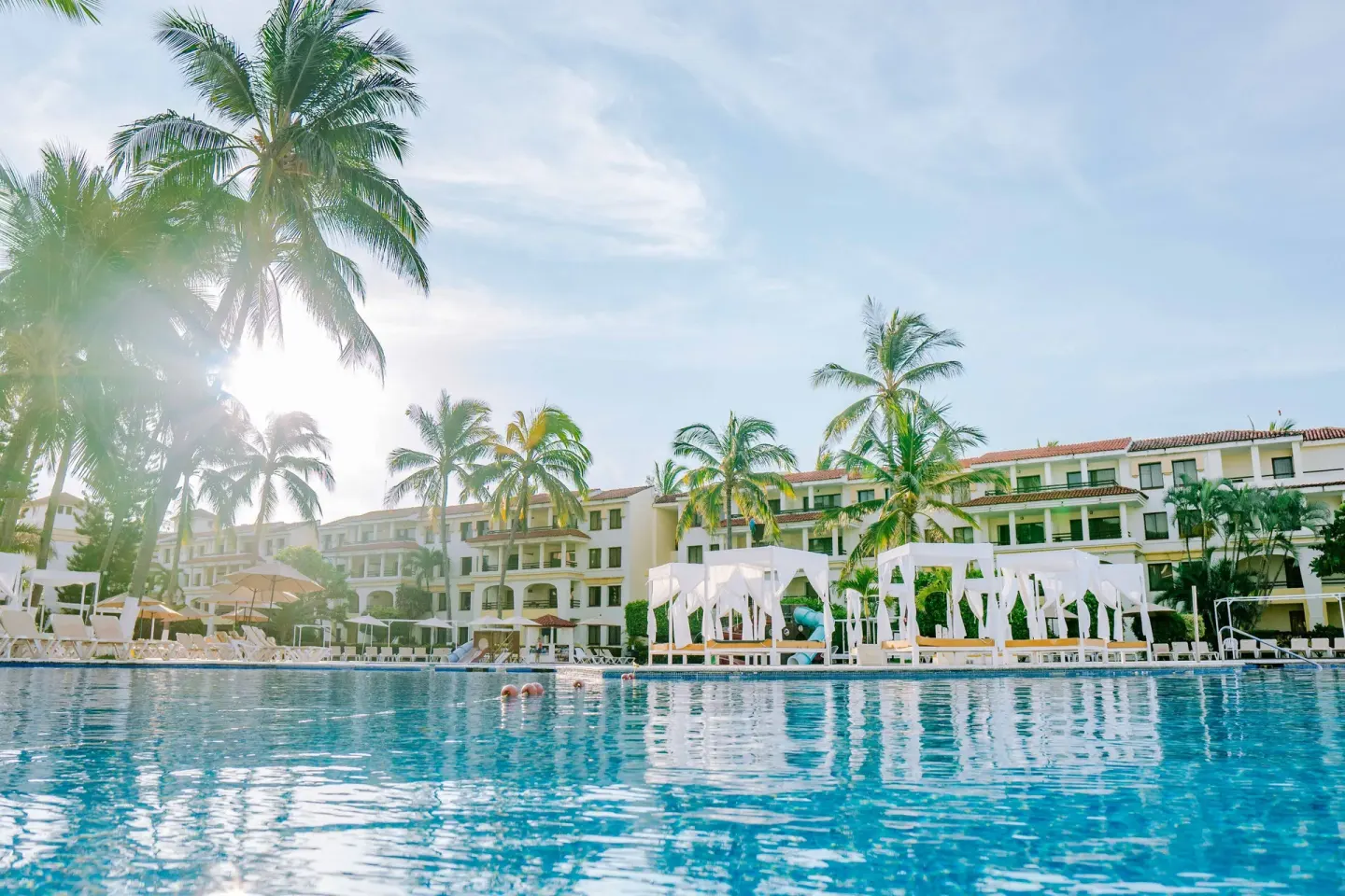 Resort pool with cabanas, palms, loungers, and guest buildings at Samba Vallarta.