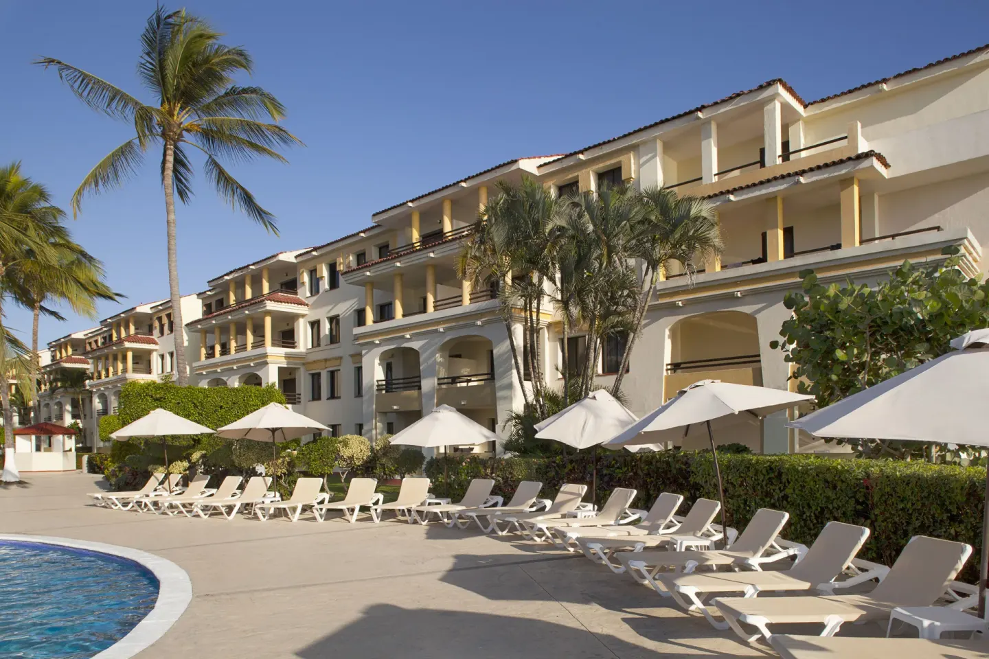 Poolside loungers and umbrellas beside guest buildings at Samba Vallarta.