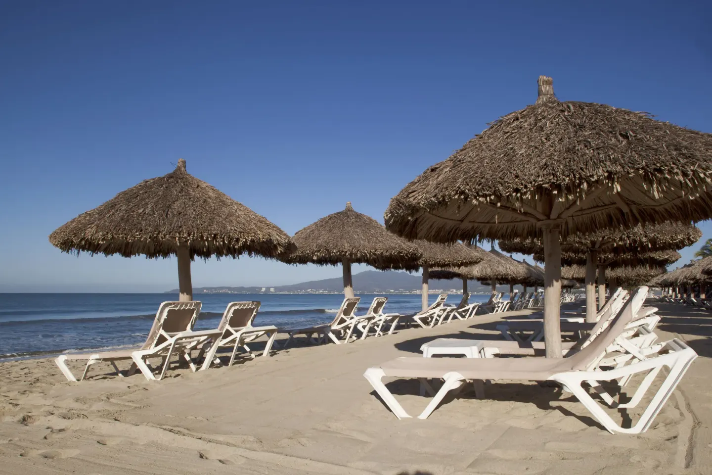 Thatched beach umbrellas and white loungers facing the ocean at Samba Vallarta.