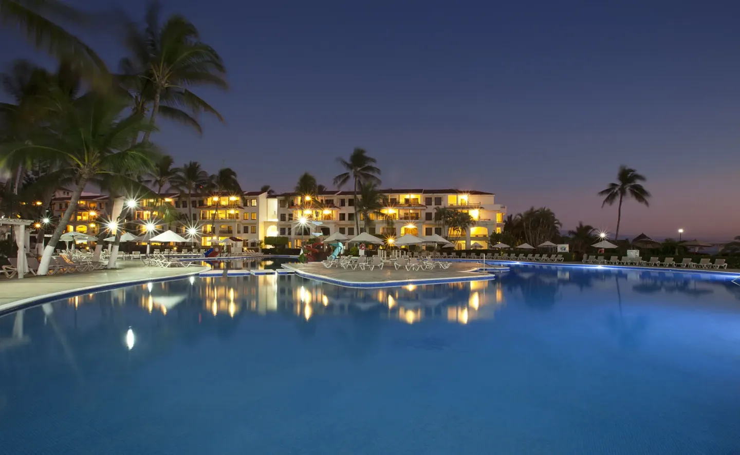 Twilight pool with lit buildings and reflections at Samba Vallarta.