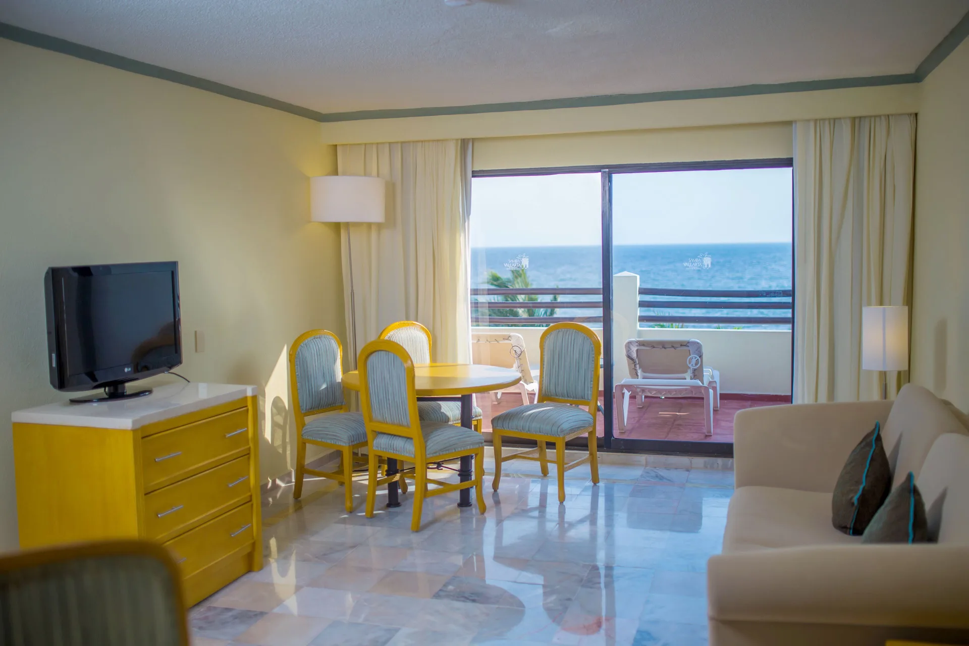 Junior Suite Ocean Front living area with sofa, dining table, TV, and balcony at Samba Vallarta.
