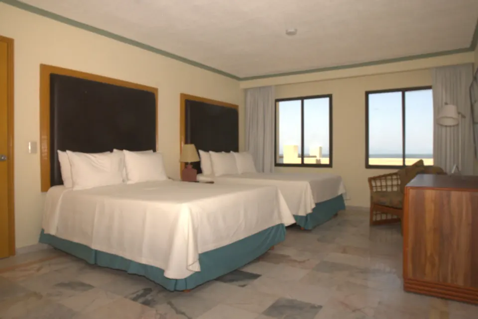 Junior Suite Ocean Front bedroom at Samba Vallarta with two beds, windows, seating, and dresser.
