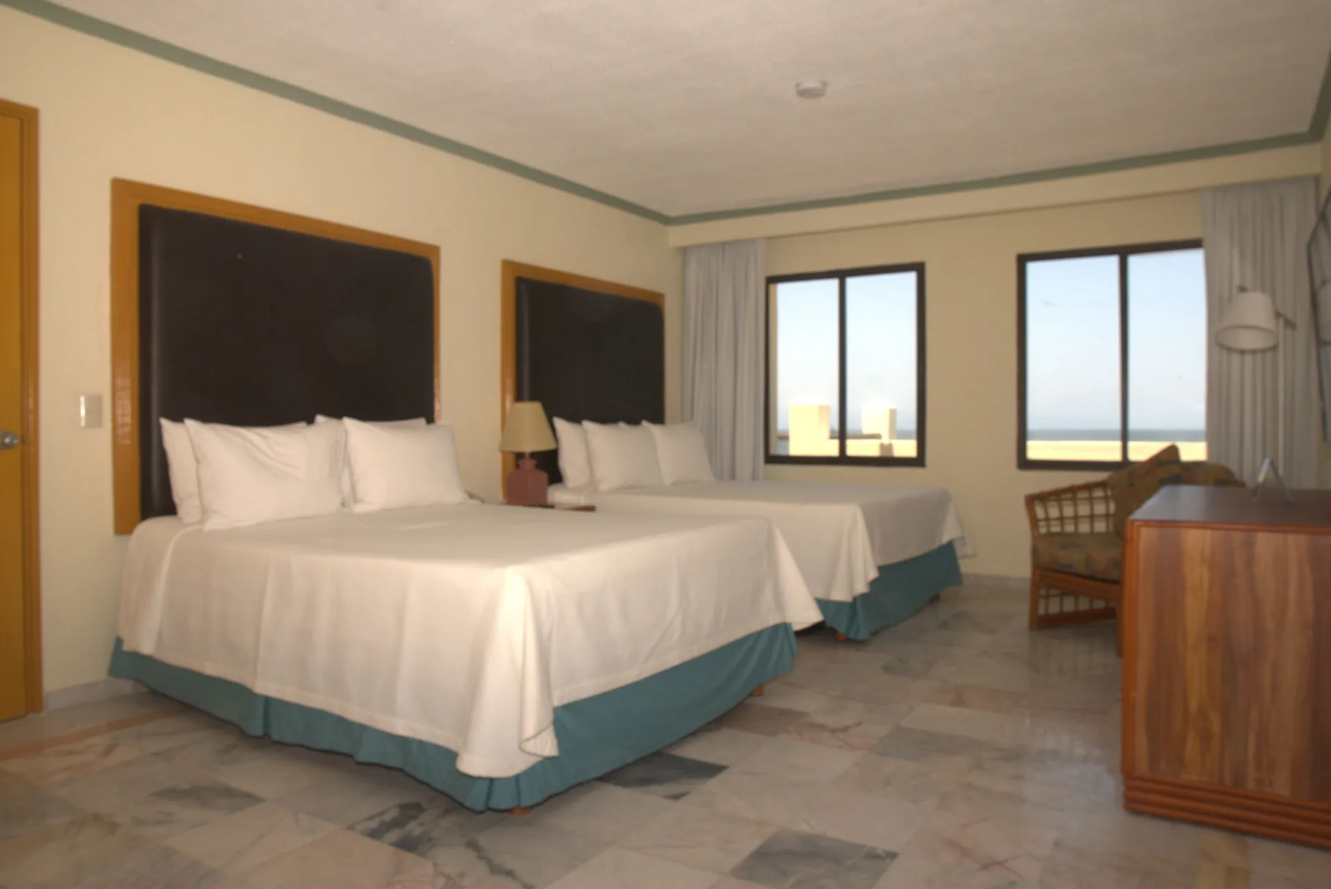 Junior Suite Ocean Front bedroom at Samba Vallarta with two beds, windows, seating, and dresser.