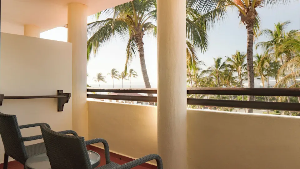 Standard Room balcony with chairs, table, columns, and palm trees at Samba Vallarta.