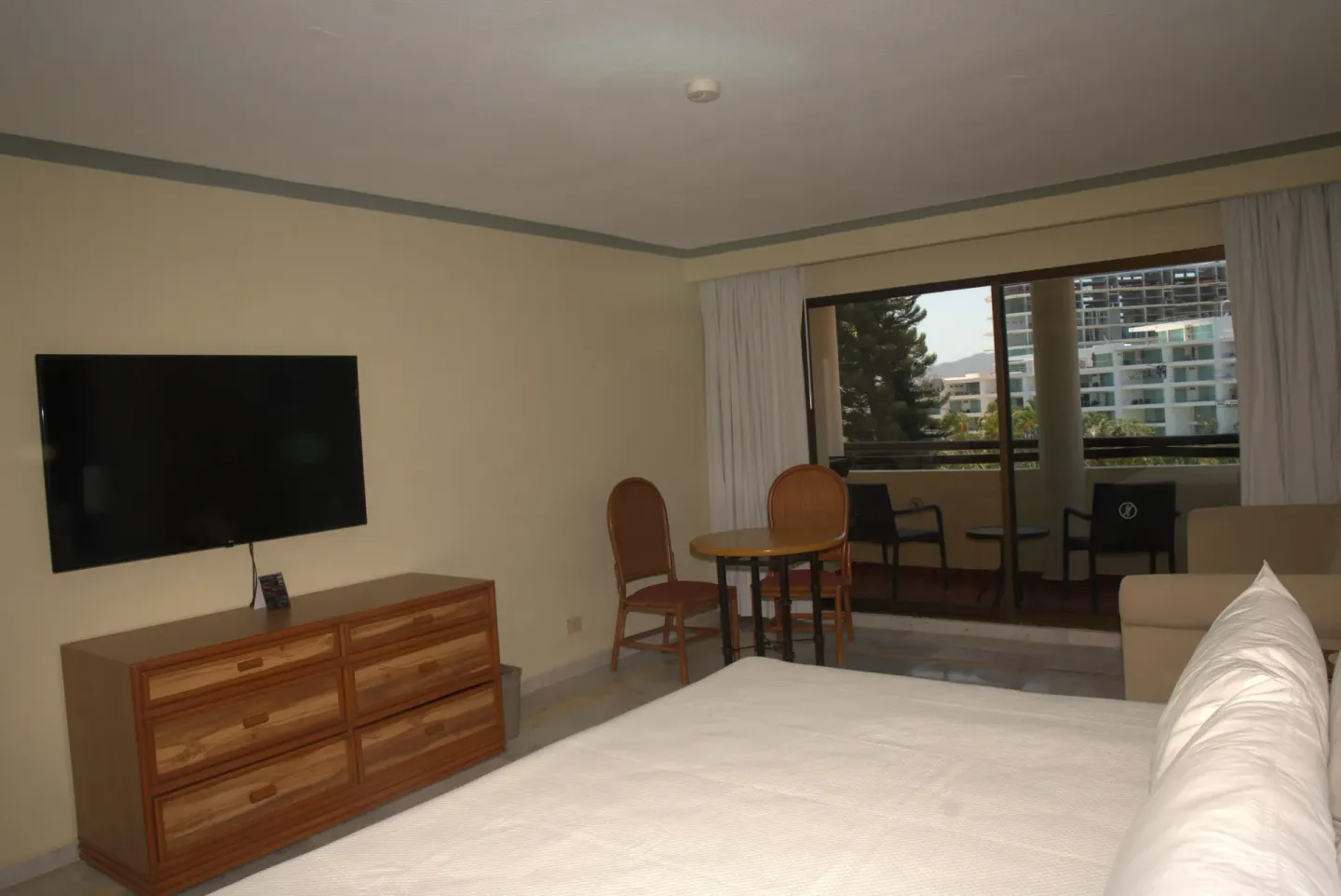 Standard Room with bed, dresser, wall-mounted TV, table, and balcony at Samba Vallarta.