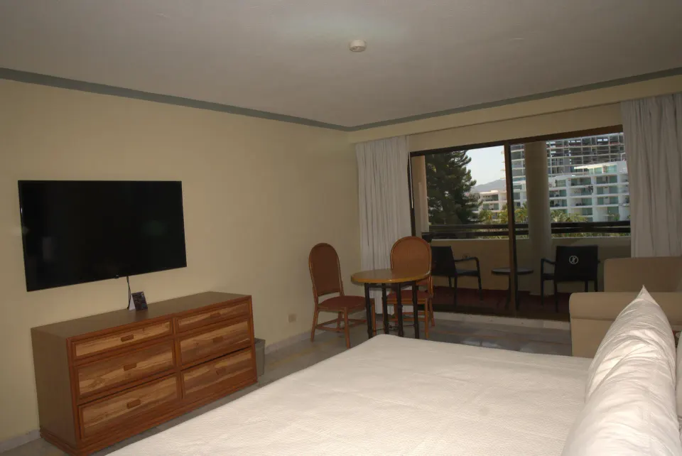 Standard Room with bed, dresser, wall-mounted TV, table, and balcony at Samba Vallarta.