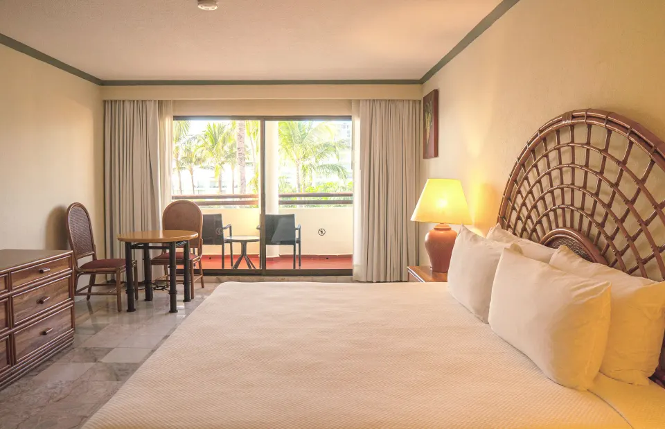 Standard Room with king bed, woven headboard, table, dresser, and balcony at Samba Vallarta.