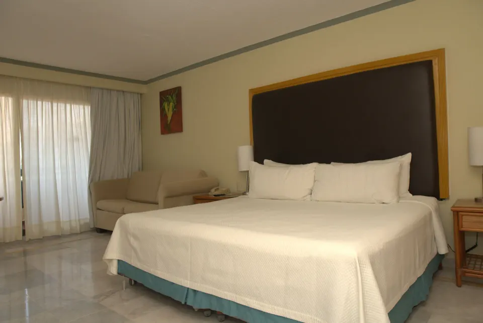 Standard Room with one bed, sofa, and curtained balcony doors at Samba Vallarta.