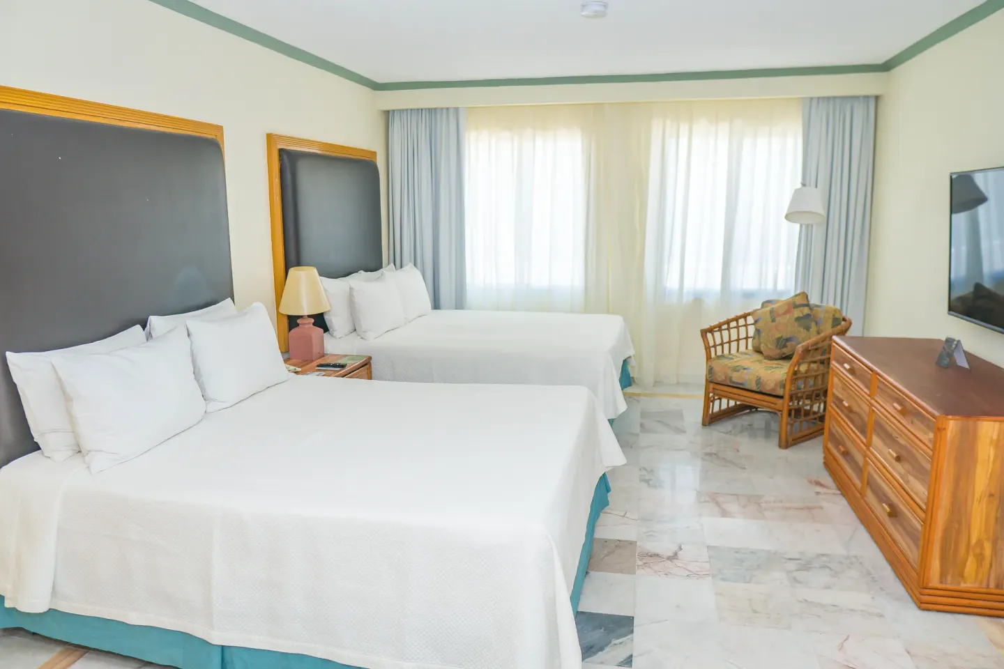 Standard Room with two beds, TV, dresser, and wicker chair at Samba Vallarta.