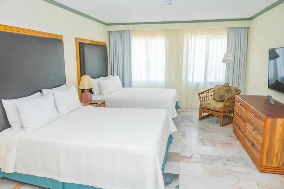 Standard Room with two beds, TV, dresser, and wicker chair at Samba Vallarta.