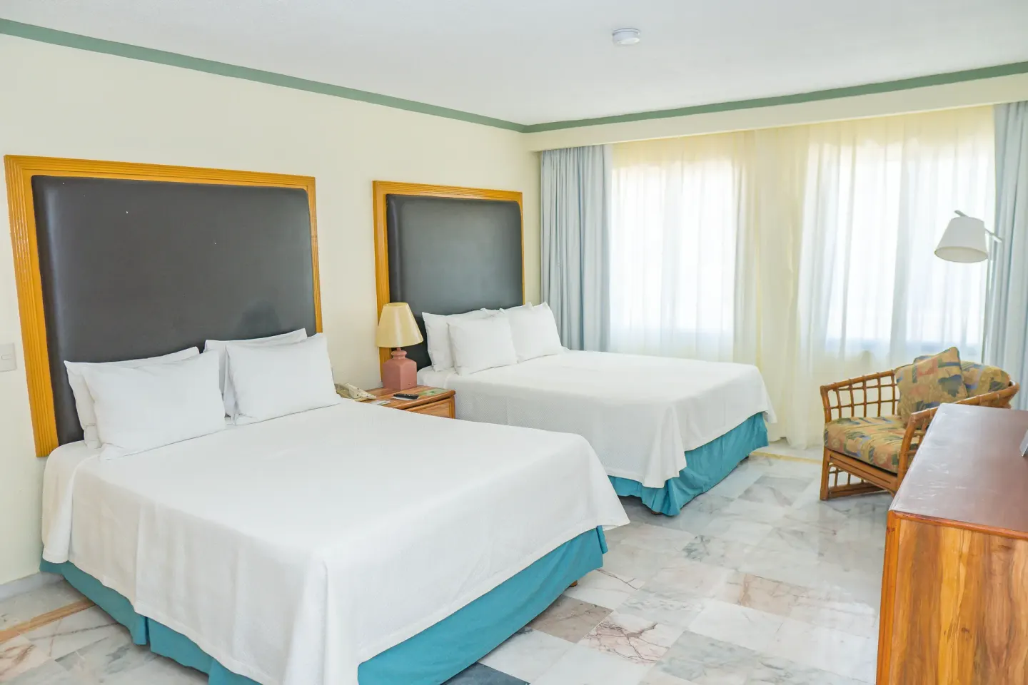 Standard Room with two beds, wicker chair, and bright window at Samba Vallarta.