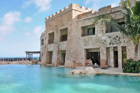 Stone castle-style building by a turquoise pool at Sanctuary Cap Cana, a Luxury Collection Resort.