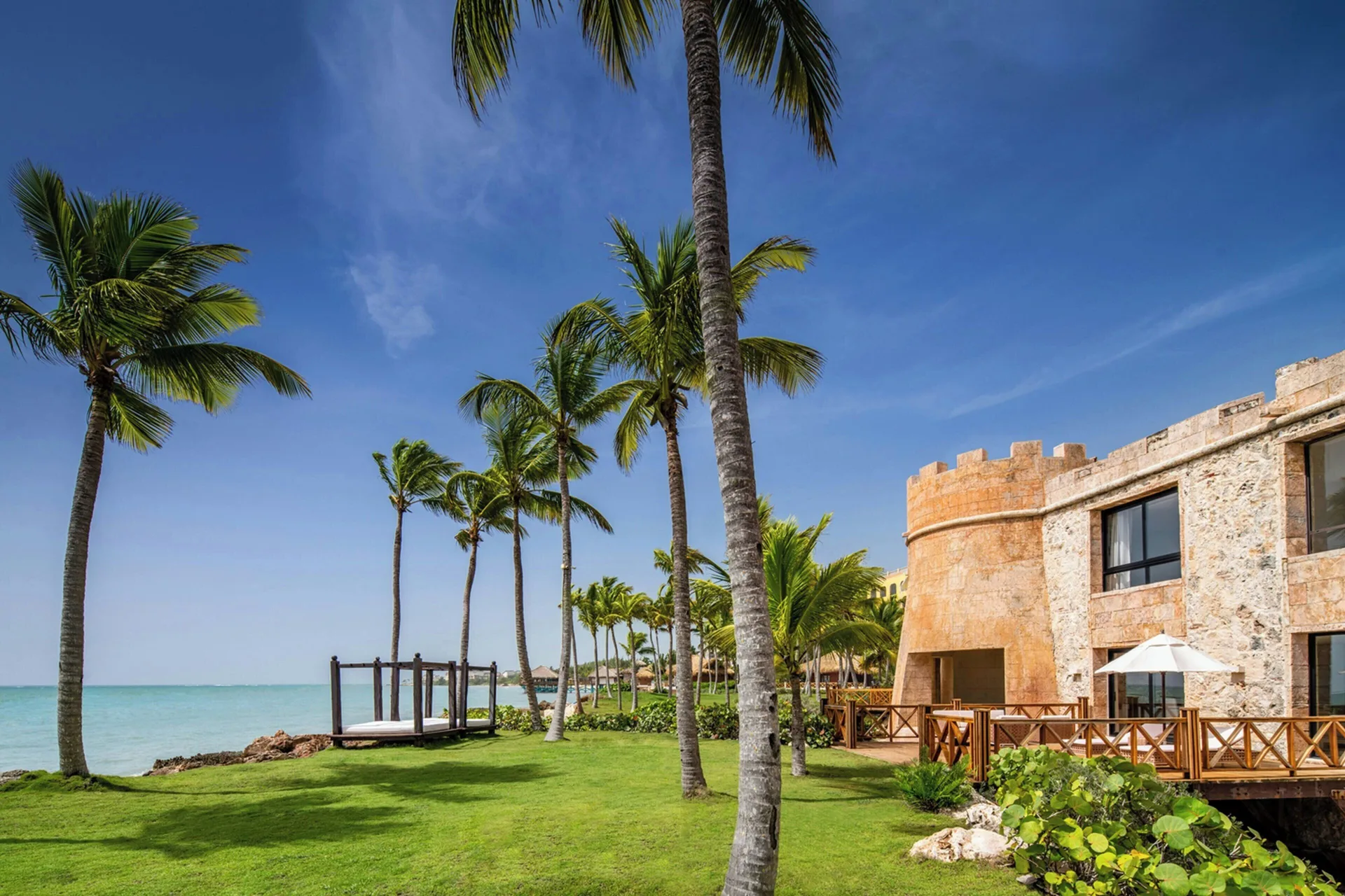 Palm-lined oceanfront lawn and stone building at Sanctuary Cap Cana, a Luxury Collection Resort.