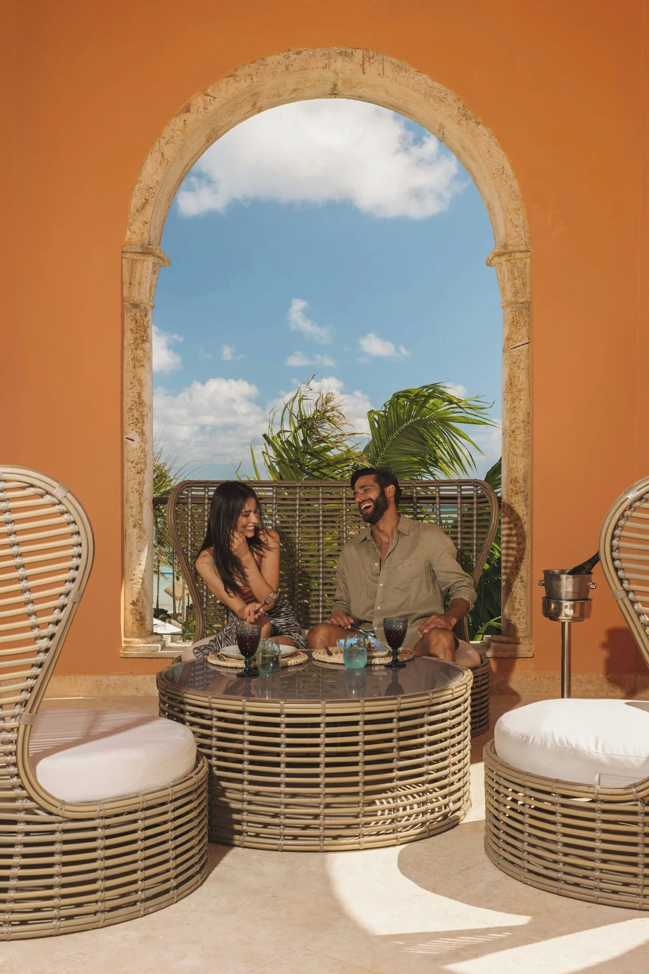 Guests sit in wicker lounge chairs by an arched window at Sanctuary Cap Cana, a Luxury Collection Resort.