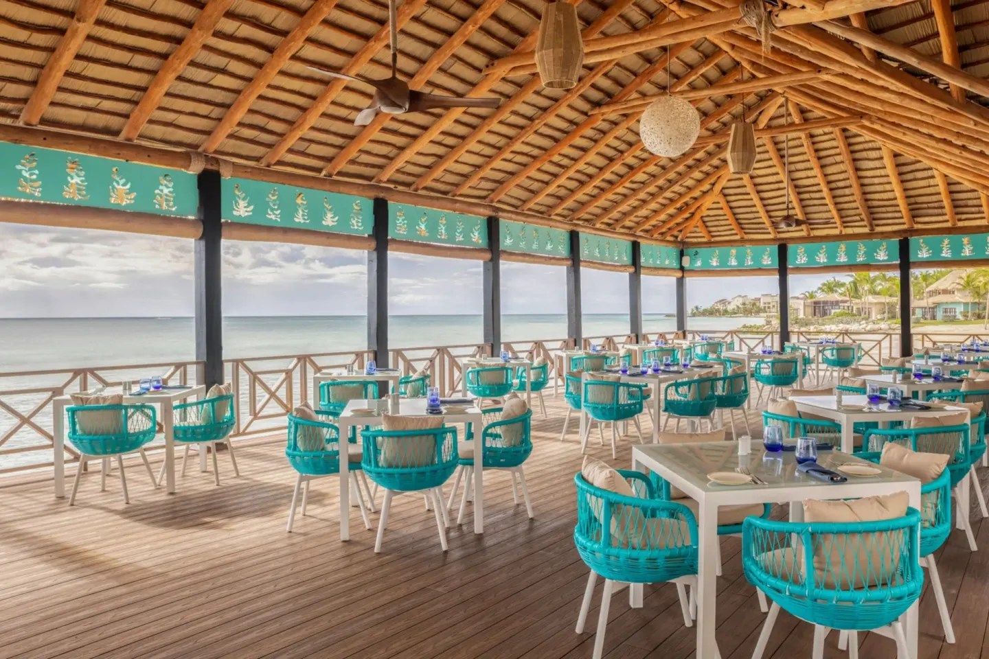 Oceanfront dining deck with turquoise chairs at Sanctuary Cap Cana, a Luxury Collection Resort.