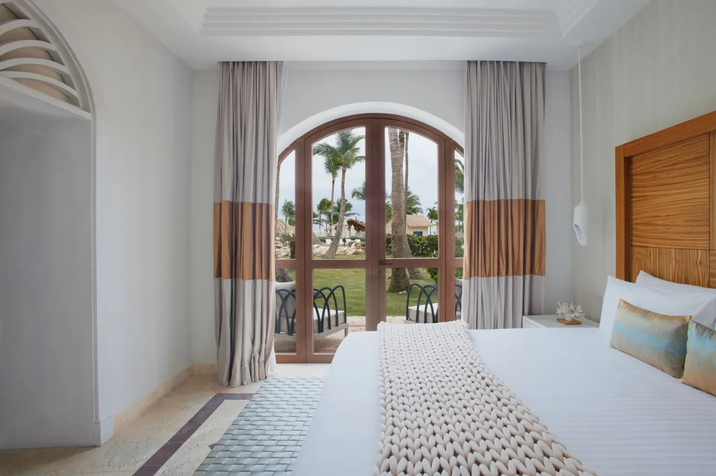 Junior Suite Beachfront king bed facing arched doors and palms at Sanctuary Cap Cana, a Luxury Collection Resort.