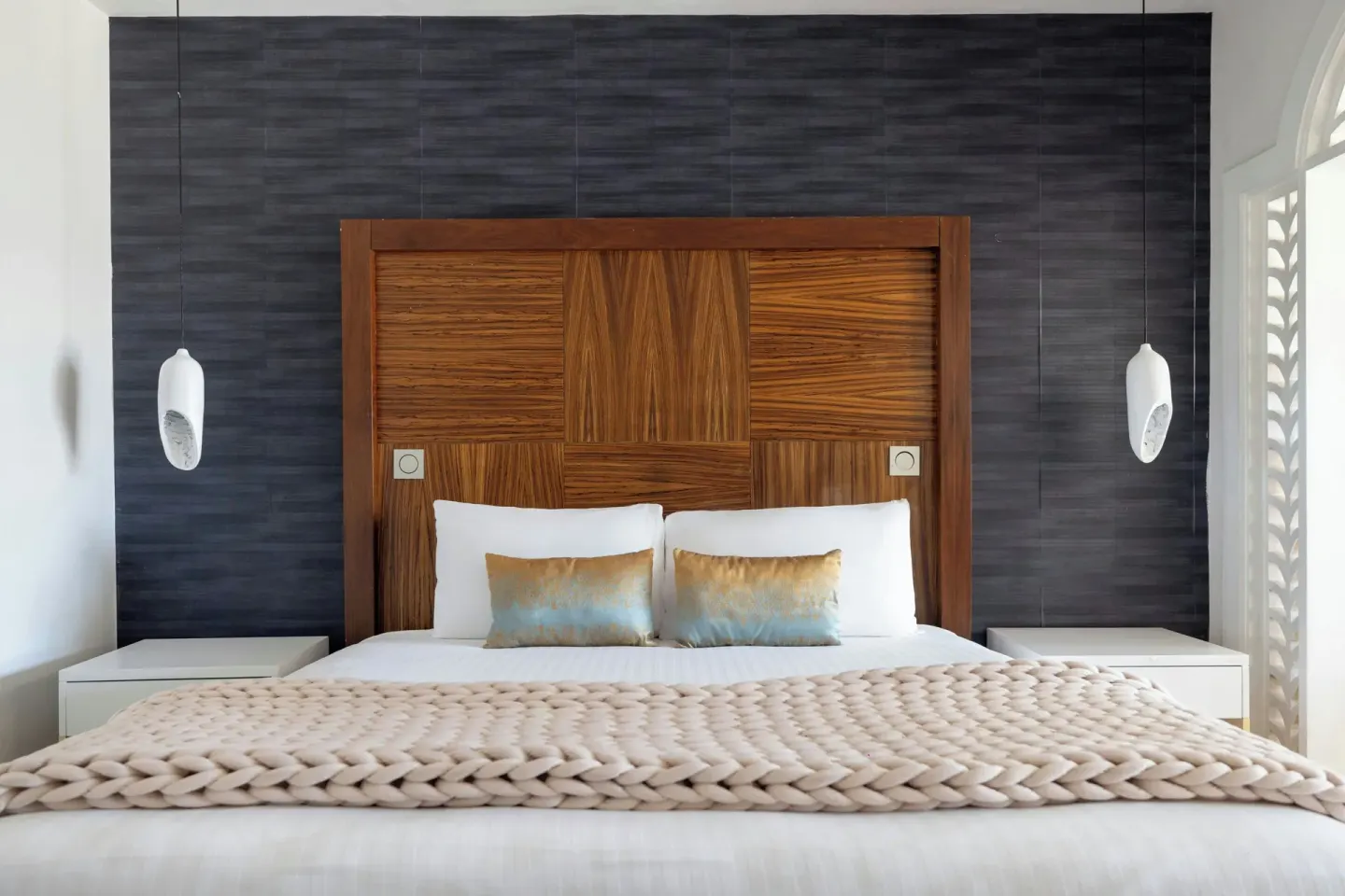 Junior Suite king bed at Sanctuary Cap Cana, a Luxury Collection Resort with wood headboard, pendant lights, and blue wall.