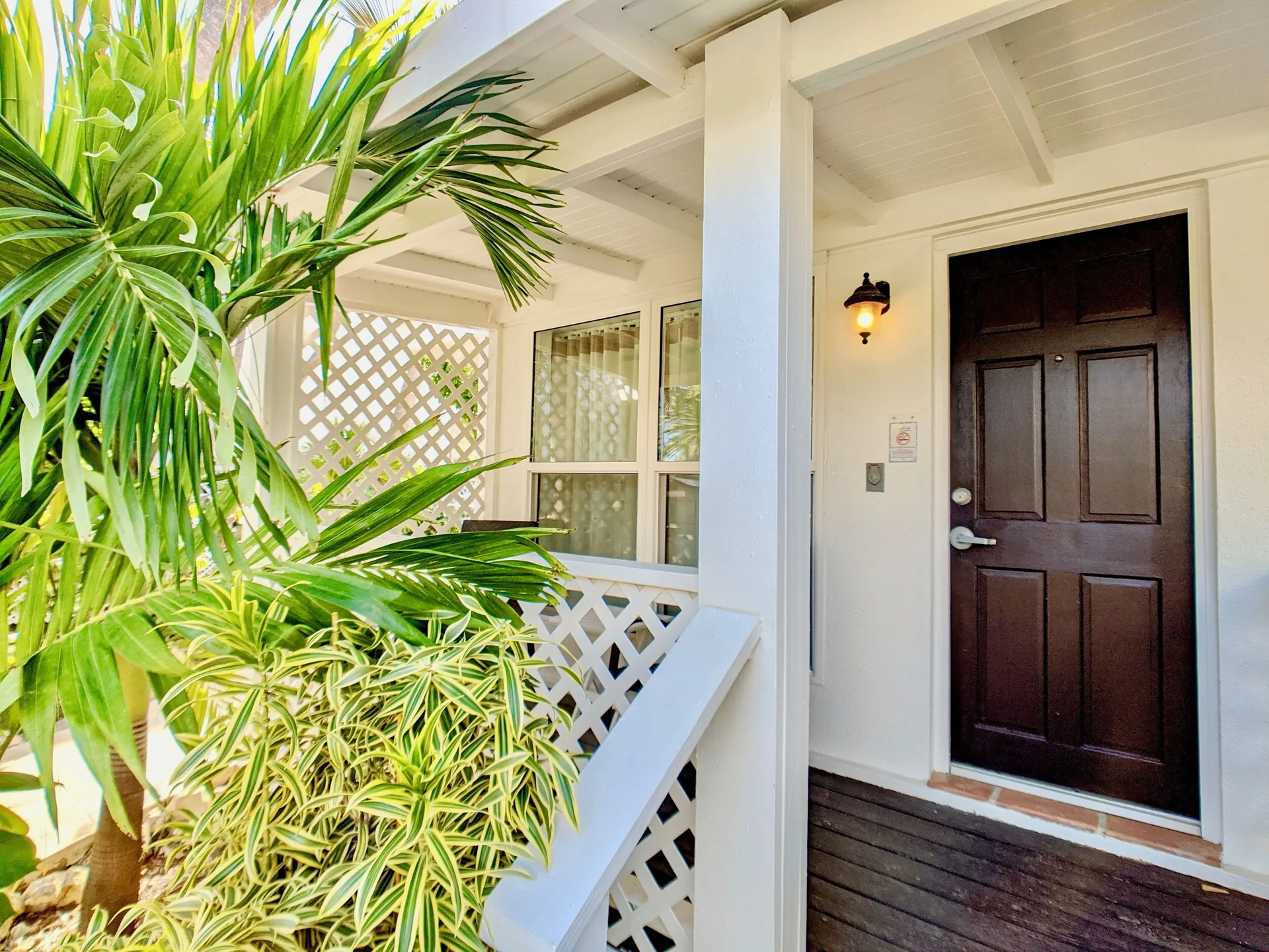 Covered guest room entry with tropical plants and a dark wood door at Sand Castle on the Beach.