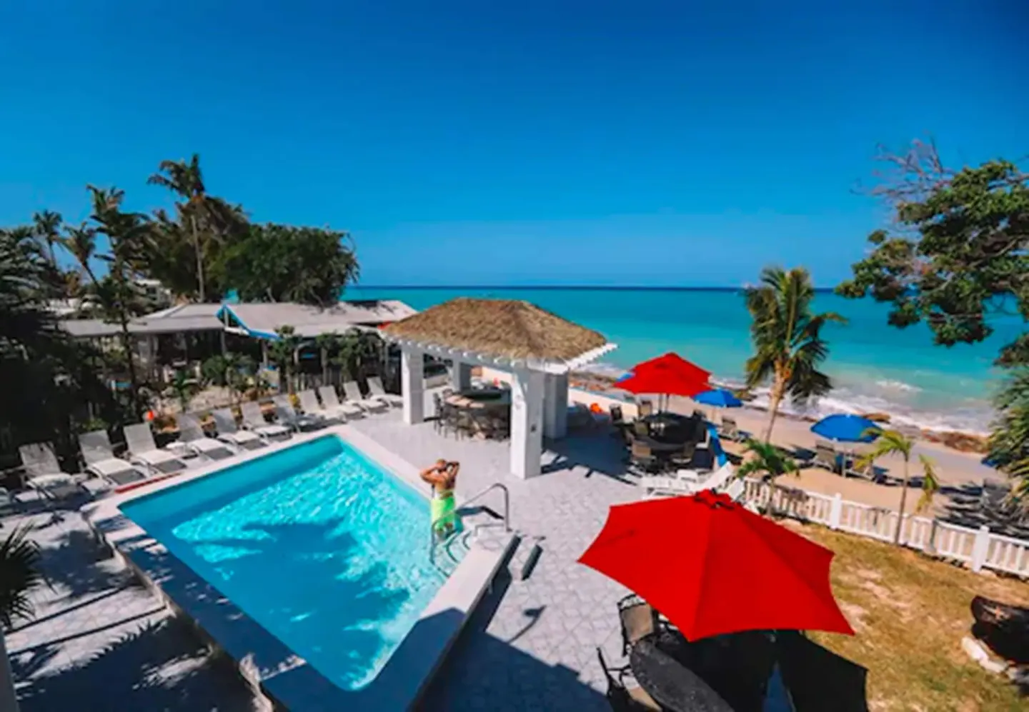 Oceanfront pool deck with loungers, red umbrellas, and turquoise sea at Sand Castle on the Beach.