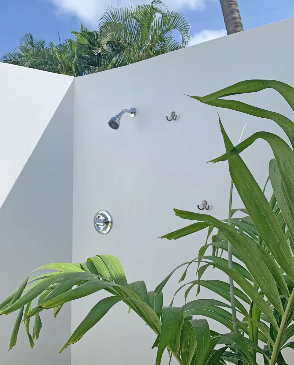 Outdoor shower with white walls and tropical plants at Sand Castle on the Beach.
