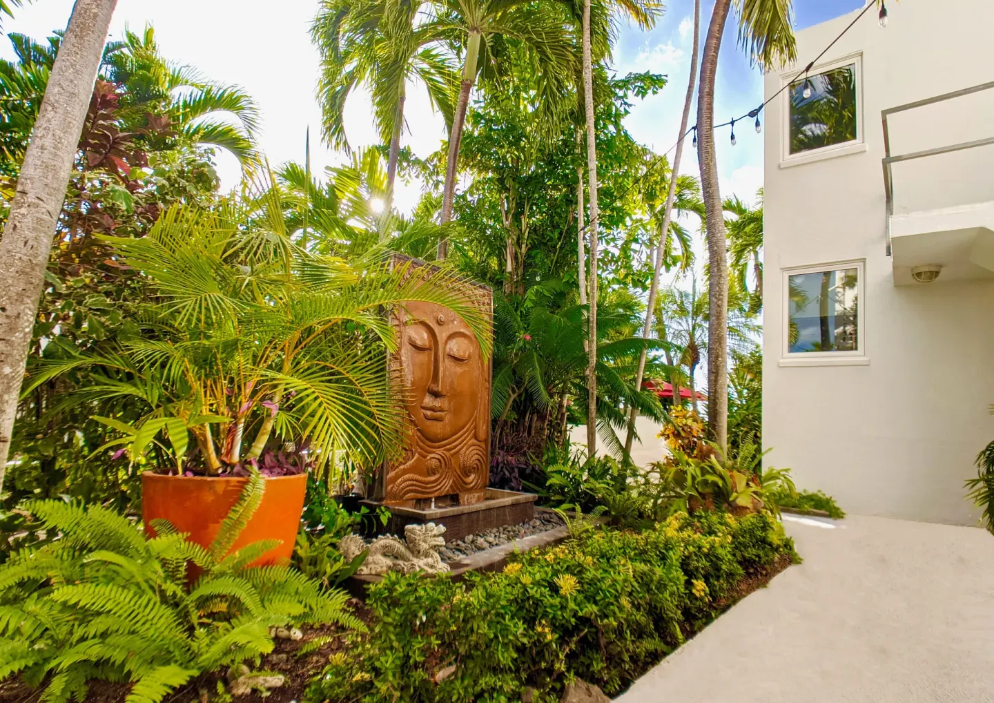 Tropical garden with a carved face fountain beside a resort building at Sand Castle on the Beach.
