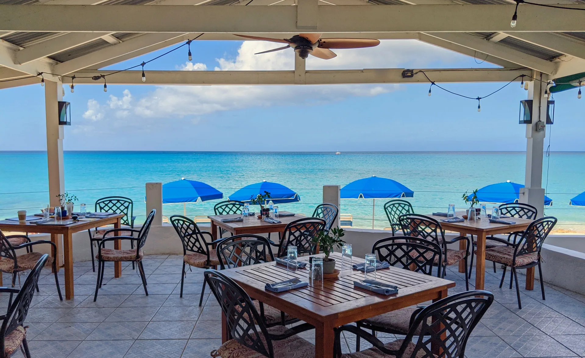 Open-air oceanfront dining tables overlooking blue water at Sand Castle on the Beach.