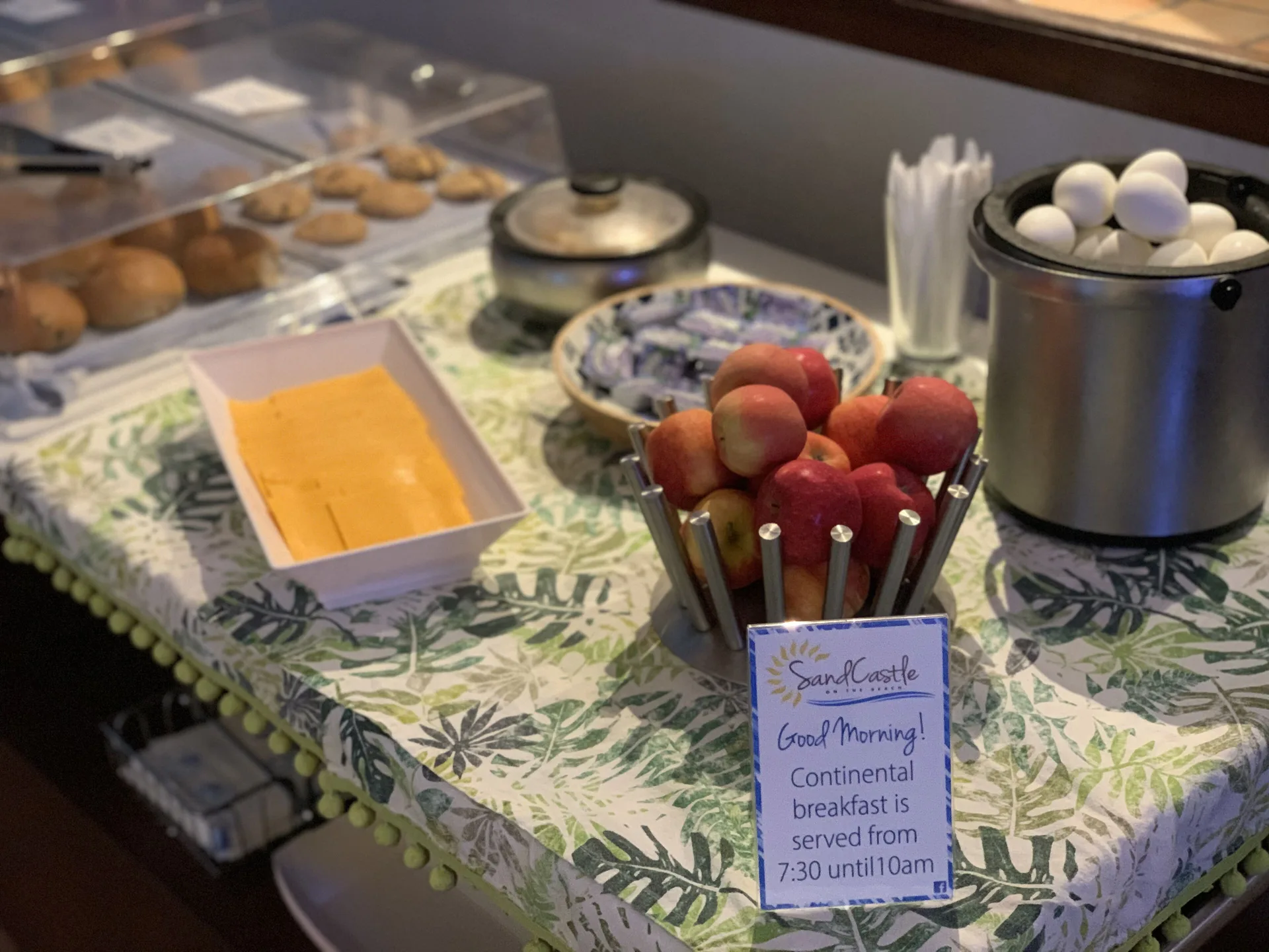 Continental breakfast display with fruit, eggs, pastries, and sign at Sand Castle on the Beach.