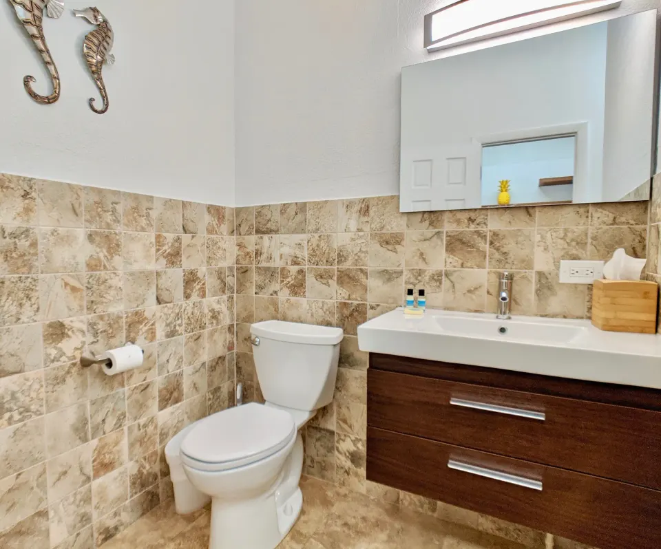 Studio Garden View bathroom vanity, toilet, mirror, and tiled walls at Sand Castle on the Beach.
