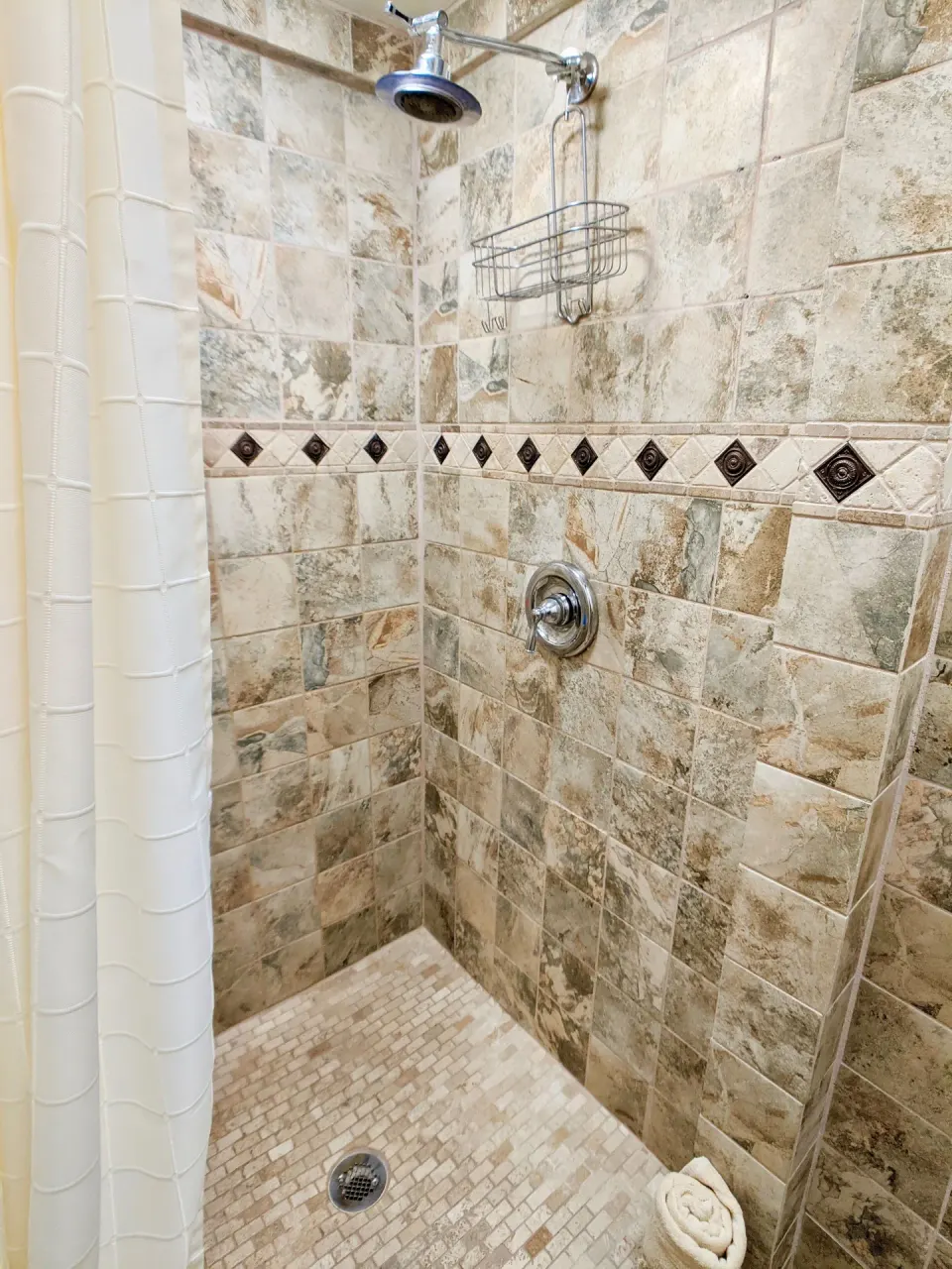 Studio Garden View tiled shower with curtain, showerhead, and wall caddy at Sand Castle on the Beach.