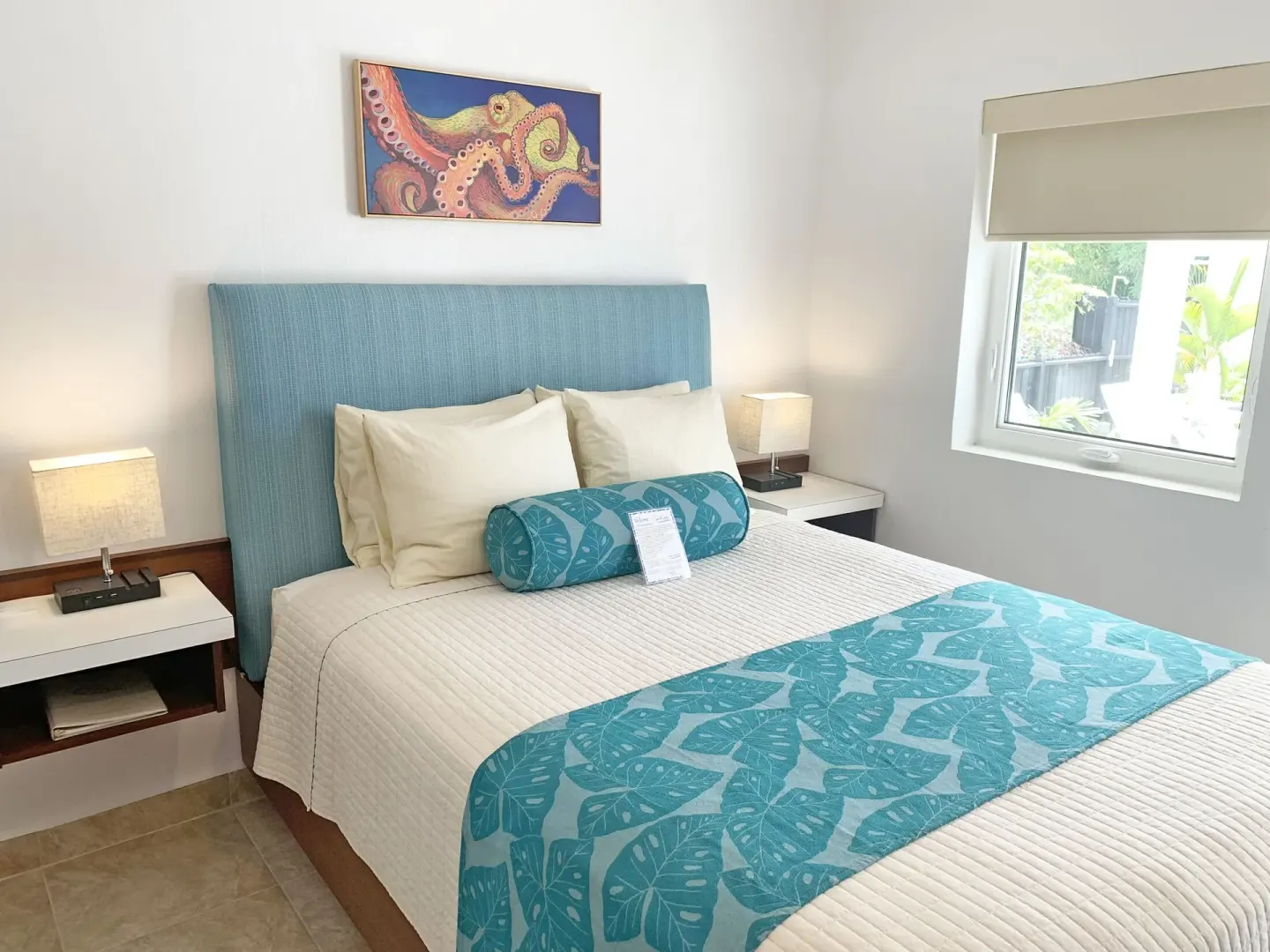 Studio guest room bed with blue accents, octopus art, and window at Sand Castle on the Beach.