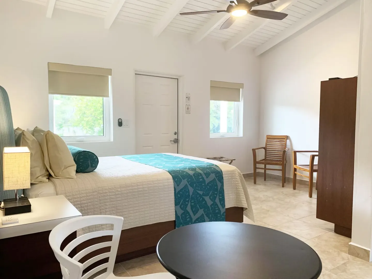 Studio guest room with bed, round table, chairs, windows, and ceiling fan at Sand Castle on the Beach.