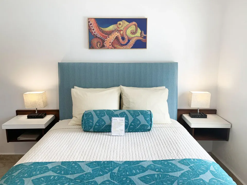 Studio guest room bed with blue headboard, lamps, and octopus artwork at Sand Castle on the Beach.