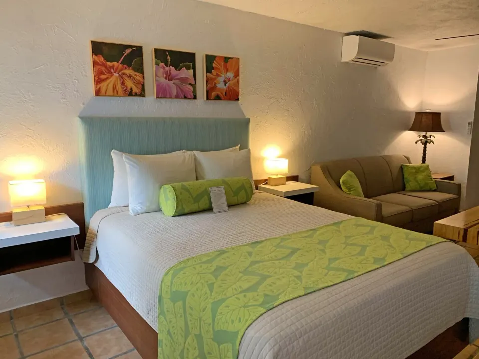 Studio guest room with bed, sofa, floral art, and wall air conditioner at Sand Castle on the Beach.