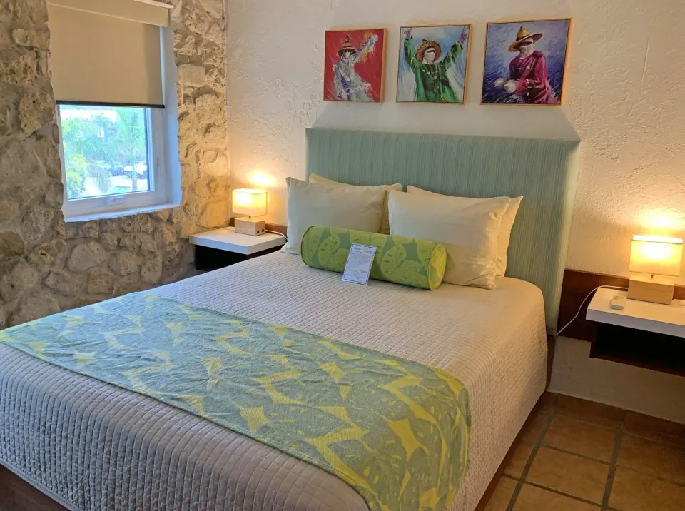 Studio guest room bed with stone wall window and bedside lamps at Sand Castle on the Beach.