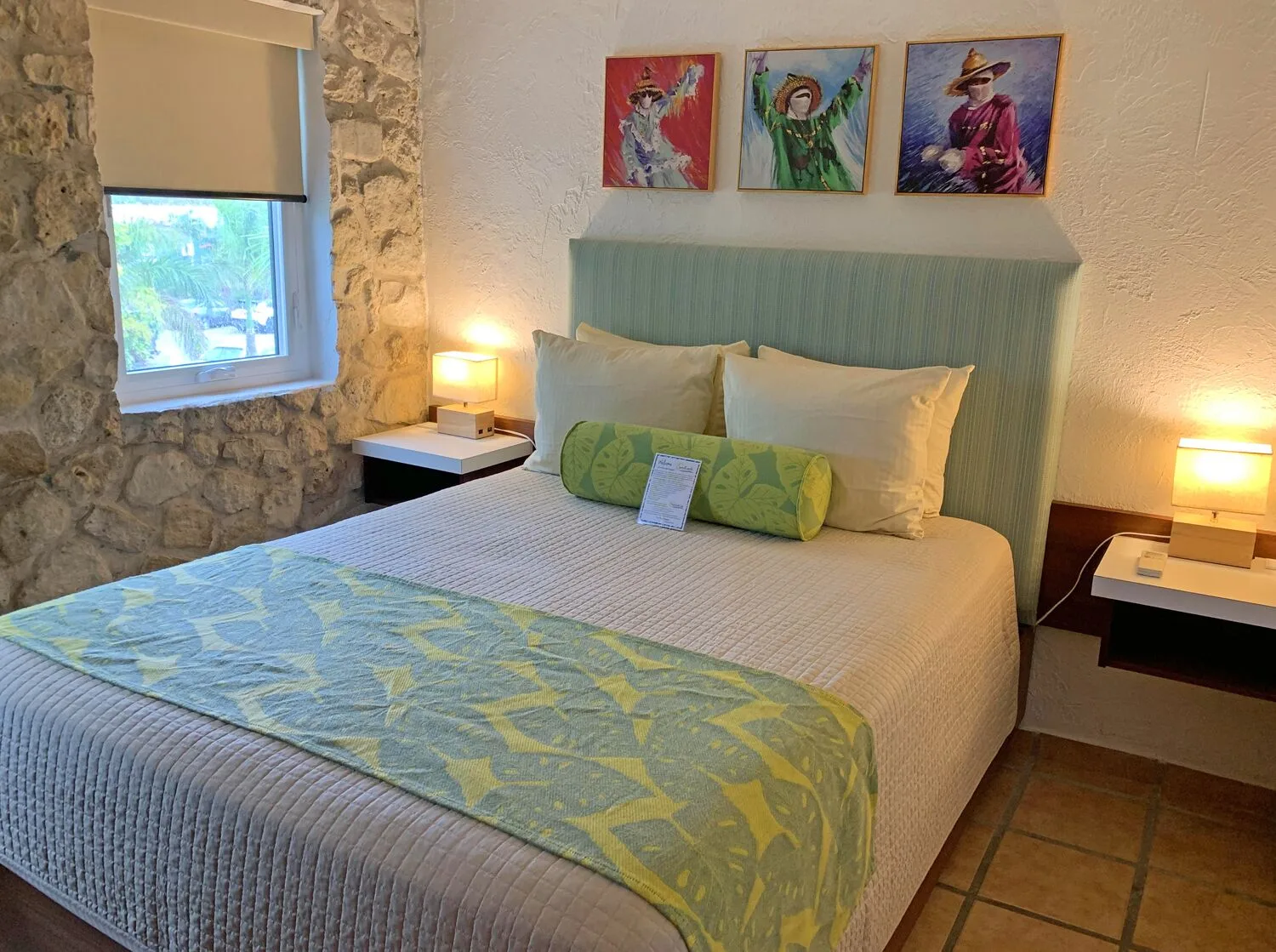 Studio guest room bed with stone wall window and bedside lamps at Sand Castle on the Beach.