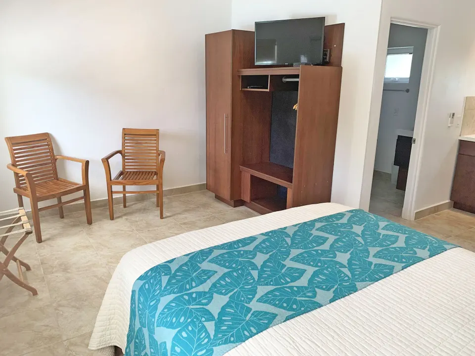 Studio guest room with bed, wardrobe, television, chairs, and bathroom doorway at Sand Castle on the Beach.