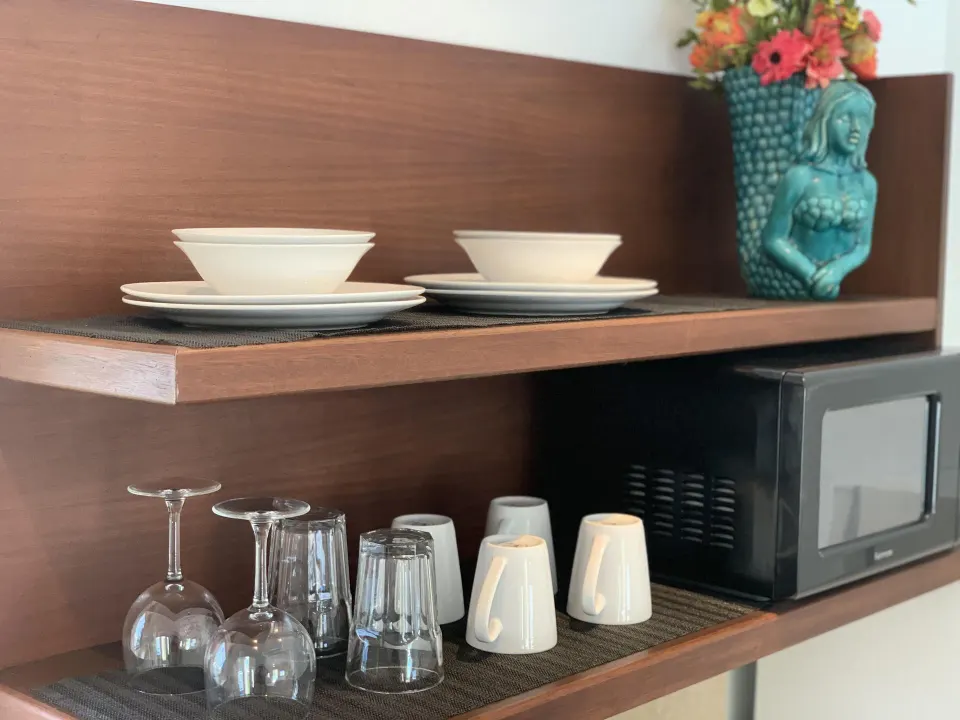 Studio kitchen shelves with dishes, mugs, glasses, microwave, and vase at Sand Castle on the Beach.